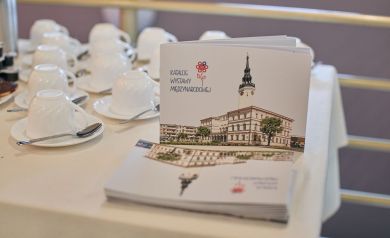 Stół z poczęstunkiem dla uczestników wystawy 'Części Całości', w tle białe filiżanki oraz uwidoczniony Katalog Wystawy Międzynarodowej 