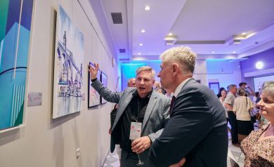 Dwóch mężczyzn podziwiający obraz przedstawiający architekturę, w tle inni uczestnicy podziwiający wystawę