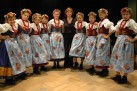 Zdjęcie grupowe zespołu tanecznego z instruktorką. Dziewczęta ubrane są w ludowe stroje. 